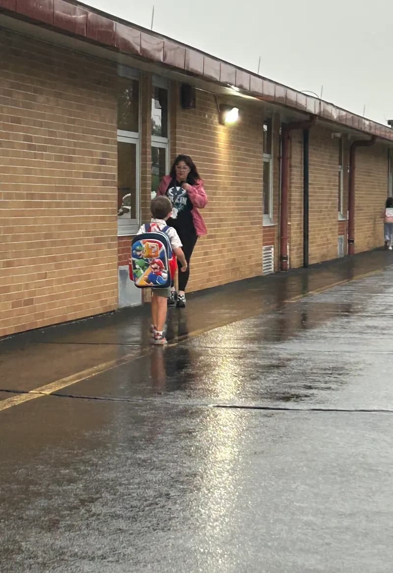 A student with a backpack walks toward an adult greeting them at the school entrance.